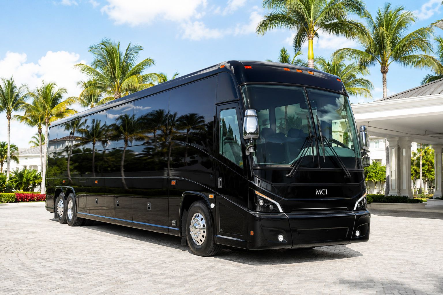 Black 55-passenger charter bus on a palm-lined driveway in South Florida