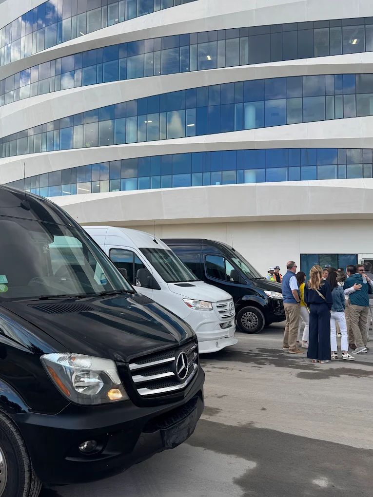 Guests gathering beside Aura Palm Sprinter vans outside a modern glass building in South Florida