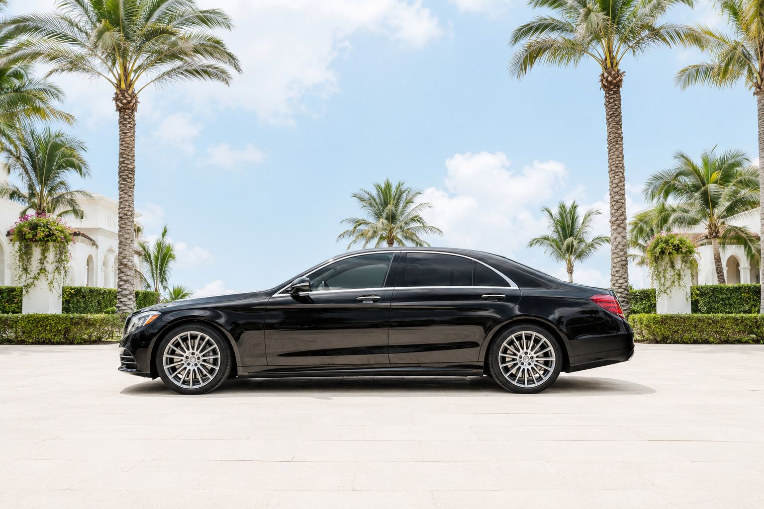 Black luxury sedan parked under tall palms at a South Florida estate