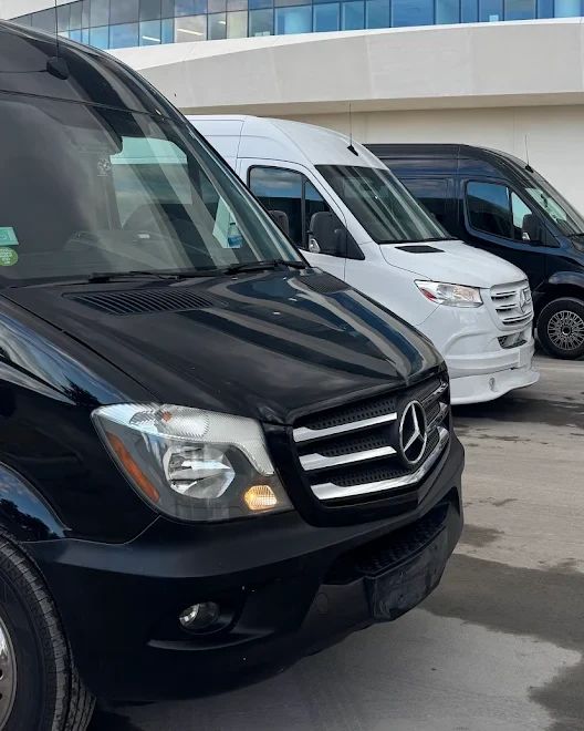 A lineup of black and white Aura Palm Sprinter vans outside a modern glass building in Miami