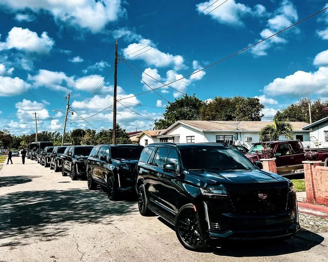 A line of black Aura Palm SUVs parked along a sunny South Florida street