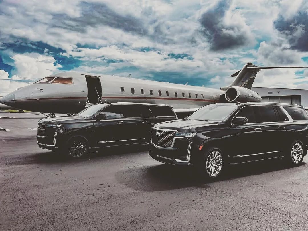 Two black Aura Palm SUVs waiting beside a private jet on the ramp